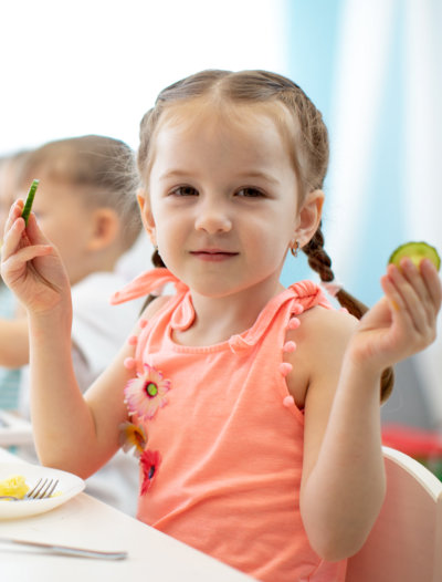 Adorable kid girl eating vegetables in kindergarten